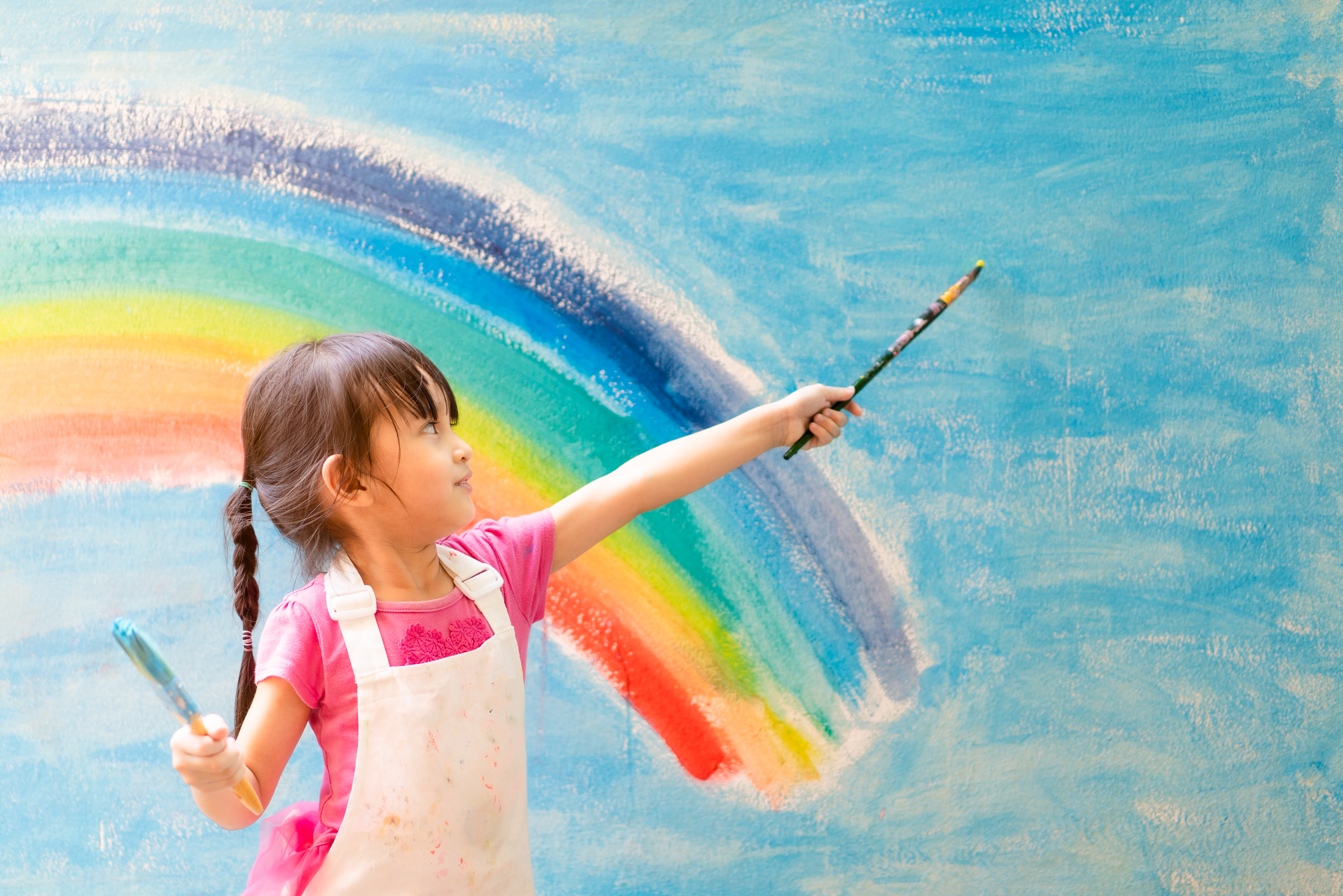 child paints rainbow on blue wall